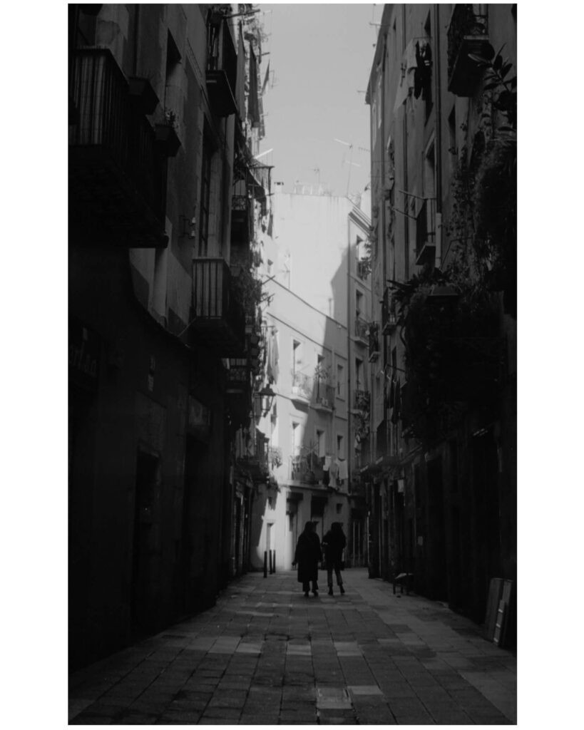 A 35mm black and white photo from Barcelona, Spain. Two women walk through a dark alley toward the light. 