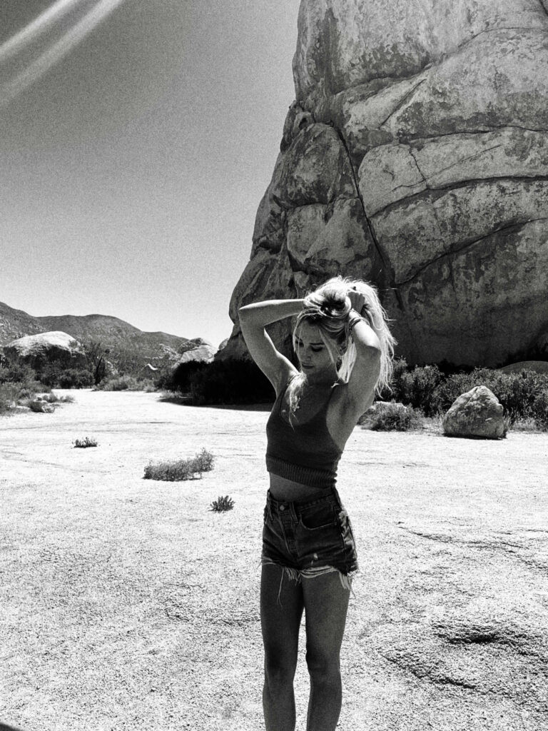 A black and white photo of Kate Ferguson standing by a rock in Joshua Tree National Park.  